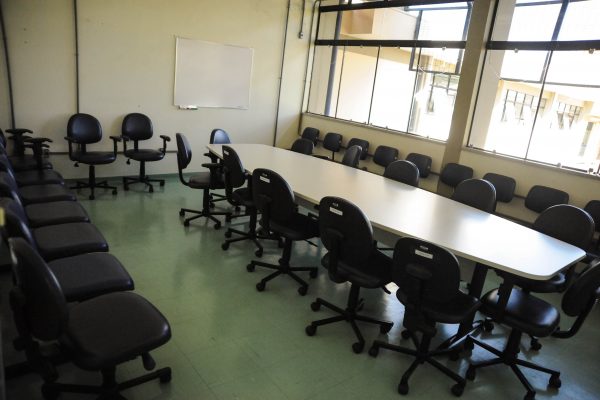 Sala de reunião com uma mesa grande e diversas cadeiras com uma lousa para pincel anatômico.